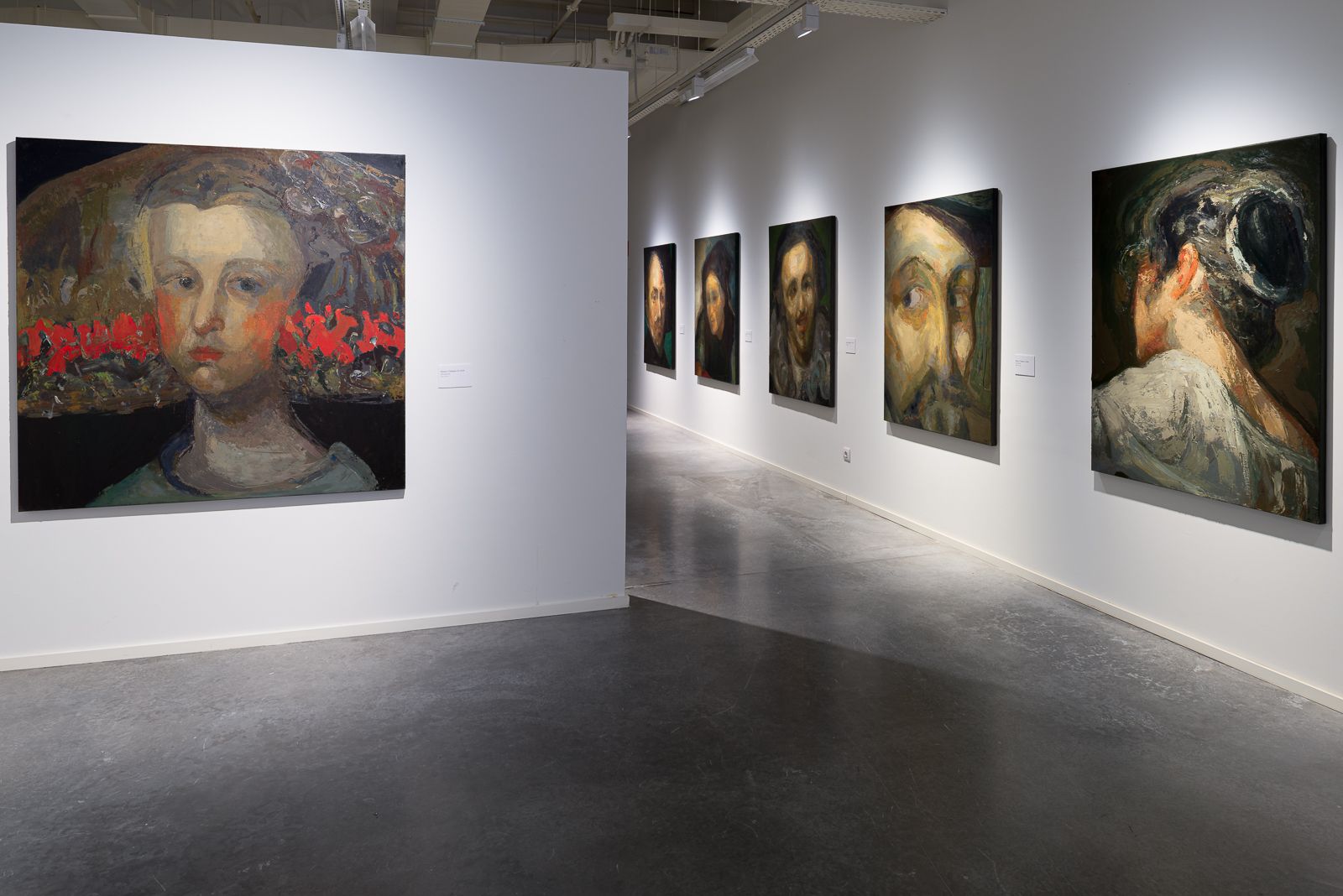 Galería de arte con retratos de Guerrero Medina en exhibición, con un gran retrato destacado en una pared divisoria blanca.