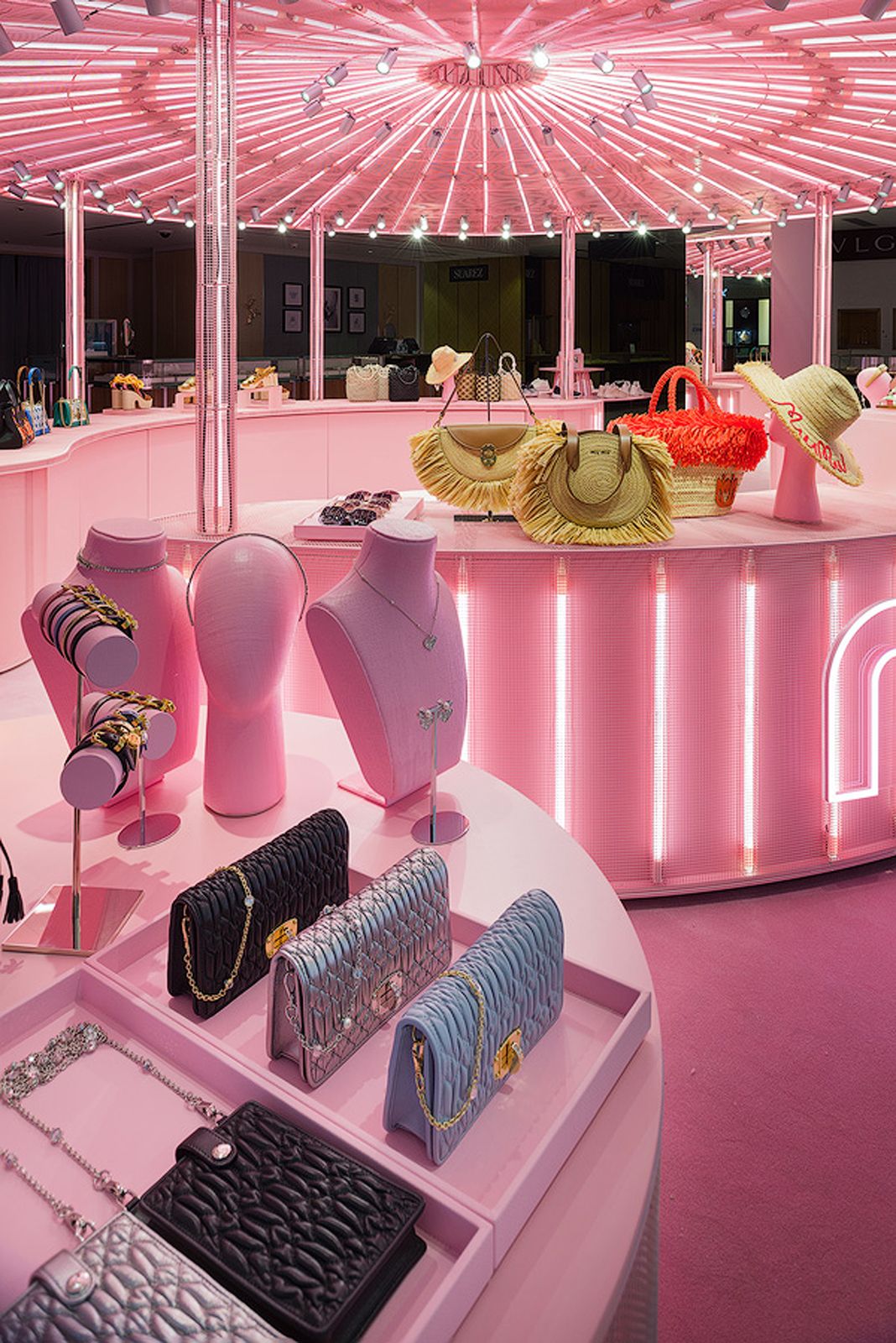 Display of Miu Miu handbags, jewelry, and hats in a brightly lit pink pop-up store.